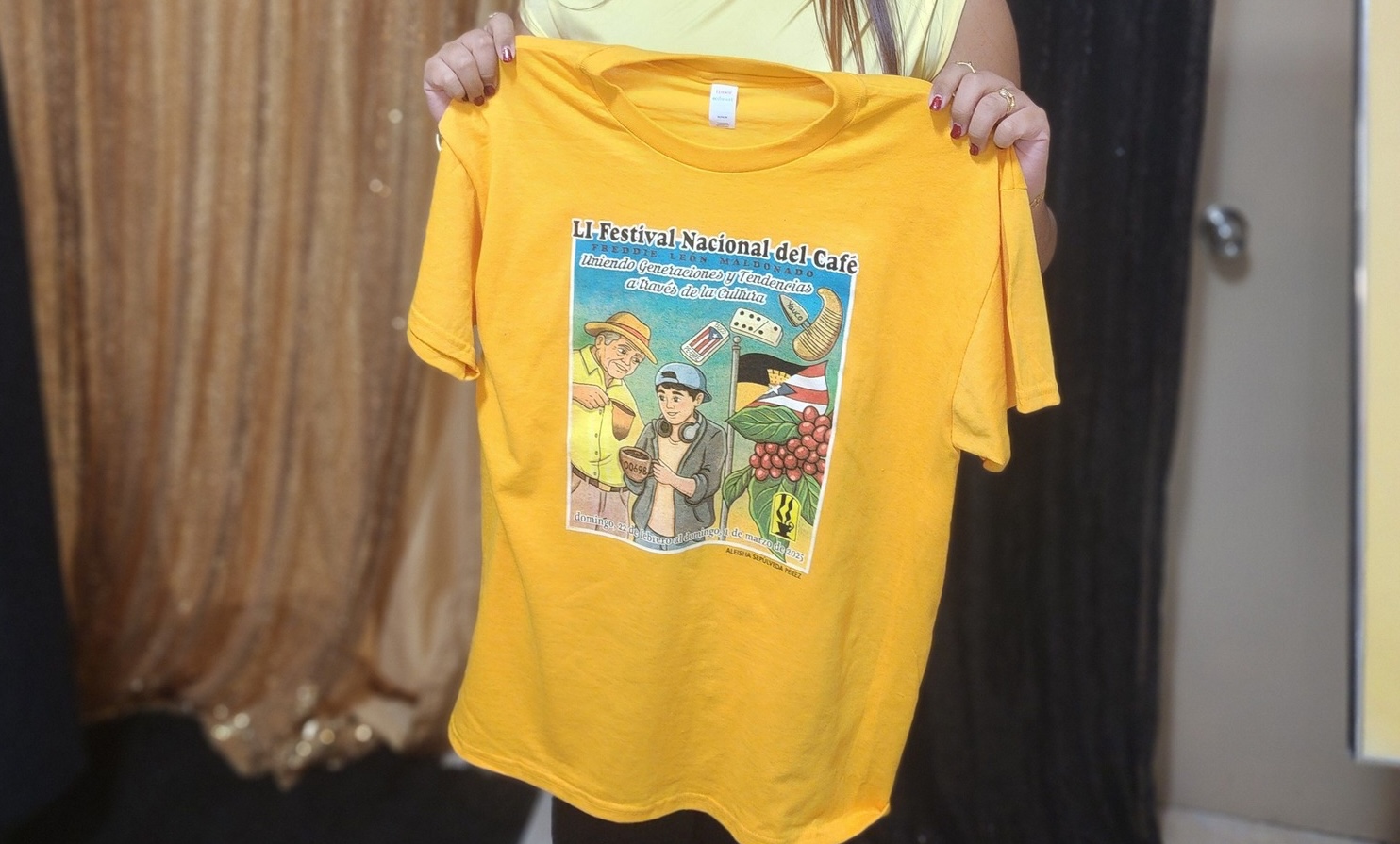 El color base de la camiseta es amarillo. La imagen muestra a dos boricuas que transmiten la tradición de la identidad puertorriqueña, especialmente a través de la vida yaucana. Combina nuestra vida local con las tradiciones puertorriqueñas nacionales.